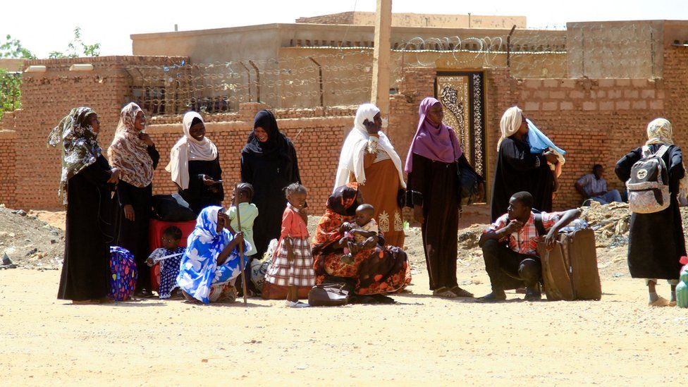 People fleeing street battles between the forces of two rival Sudanese generals, wait with their belongings along a road in the southern part of Khartoum