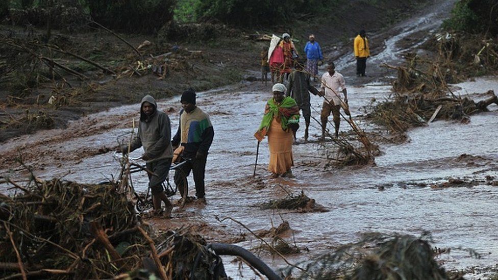 People attempt to cross the waters of a flash flood at Solai after the banks of a dam burst its banks