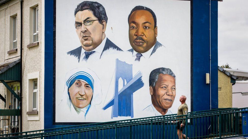 A man walks past the Bogside mural in Derry City of John Hume, Martin Luther King Jr, Mother Teresa, and Nelson Mandela
