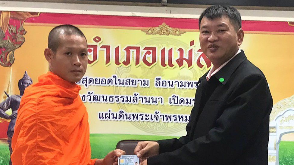 Тренер футбольной команды «Дикий кабан», ставший буддийским монахом Экапол Чантавонг (слева), когда он получает тайский удостоверение личности гражданина от главы округа Мае Сай Сомсака Канакхама (справа)