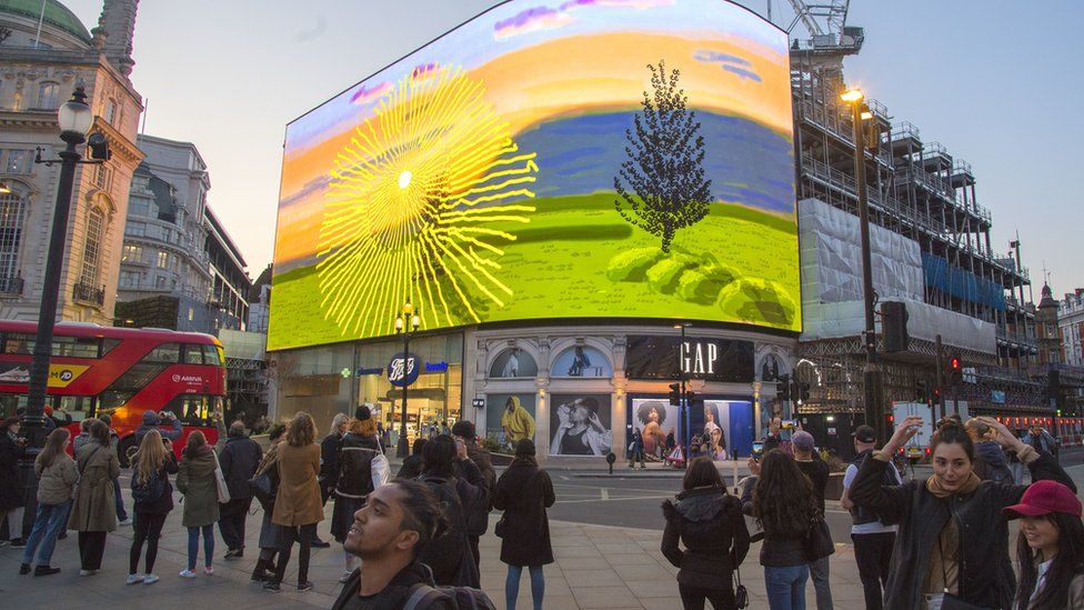 People watch the global premiere of a David Hockney artwork which is being screened on the Piccadilly Lights in