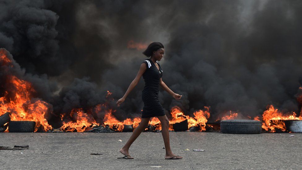 A woman walks past tire barricades set ablaze by demonstrators on the fourth day of protests in Port-au-Prince