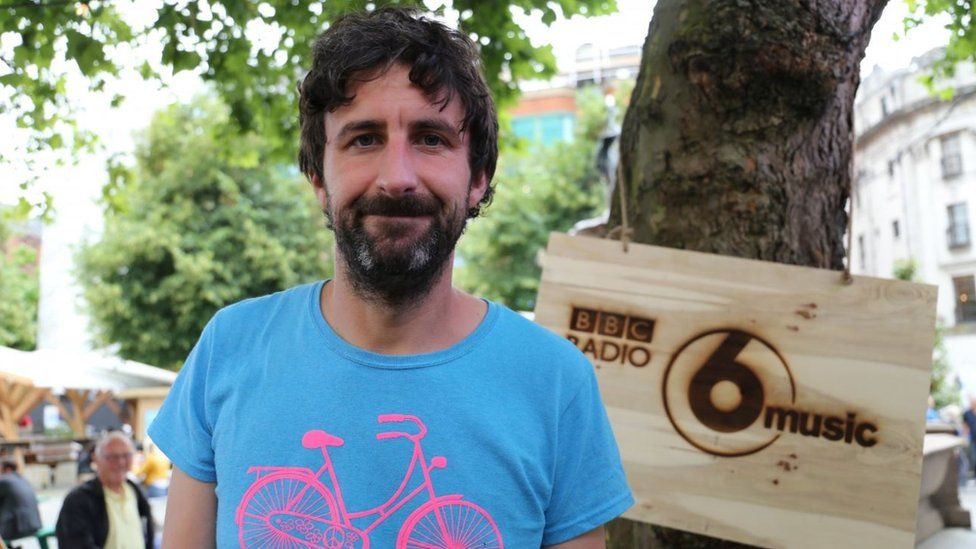 Mark Watson in front of a BBC Radio 6 Music sign