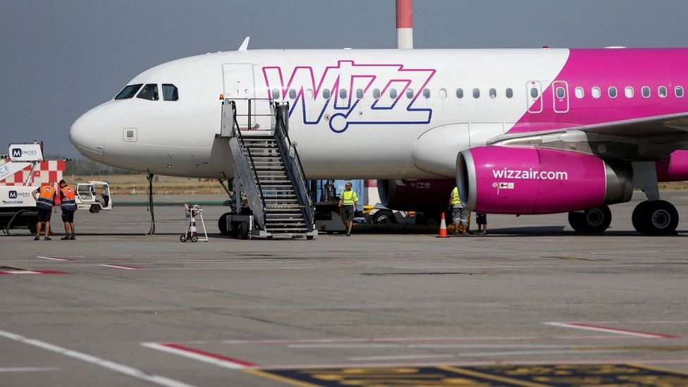 A Wizz Air branded airplane sitting on a runway with the boarding stairs still attached to it