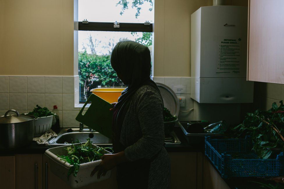 A participant holds a chopping board and bowl of vegetables in the kitchen