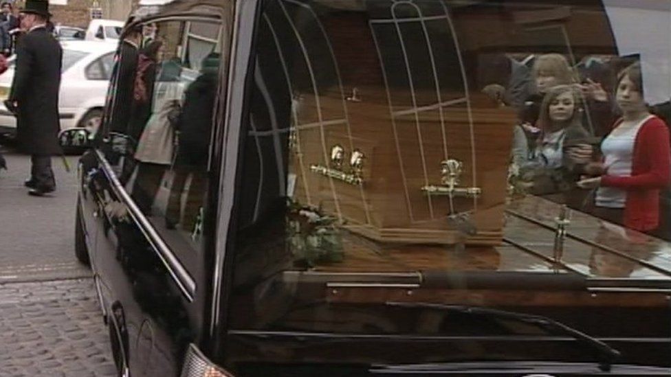 Mourners reflected in the windows of Ashok Kumar's hearse