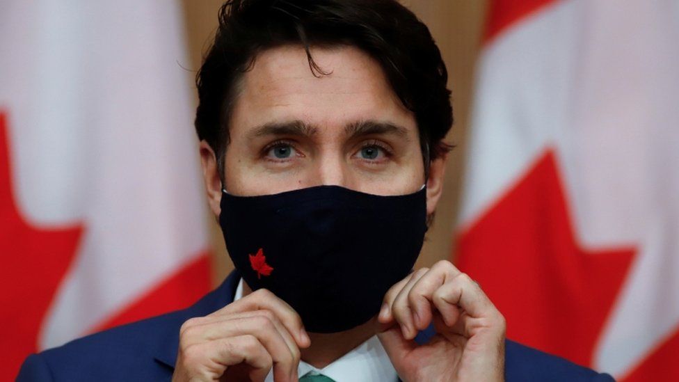 Canadian Prime Minister Justin Trudeau puts on a mask at a news conference held to discuss the country's coronavirus disease