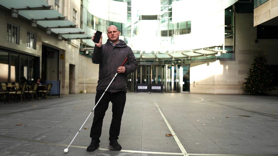 Sean Dilley holds his telephone  and achromatic  cane