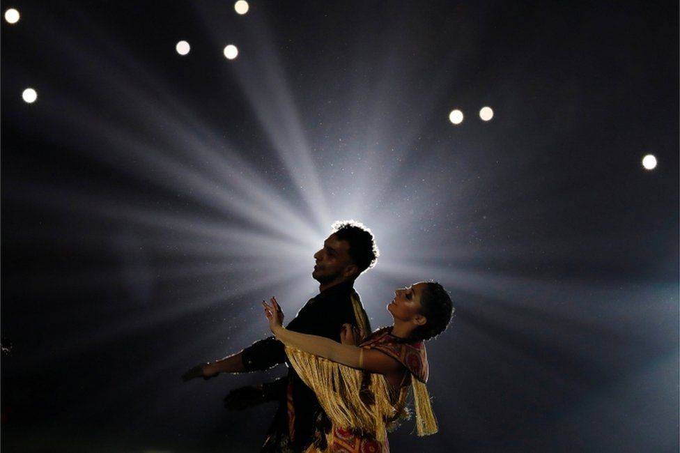 A male and female dancer perform together against a dark, dramatic backdrop