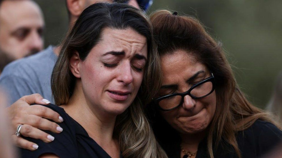 Two women cry and hold one another at a funeral for a man murdered by Hamas