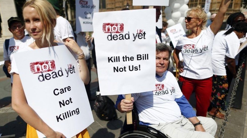 Campaigner holding placard saying Care Not Killing