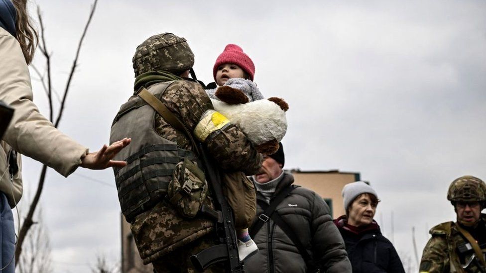 A Ukrainian serviceman carries a child while assisting people to evacuate the city of Irpin, northwest of Kyiv, 5 March 2022