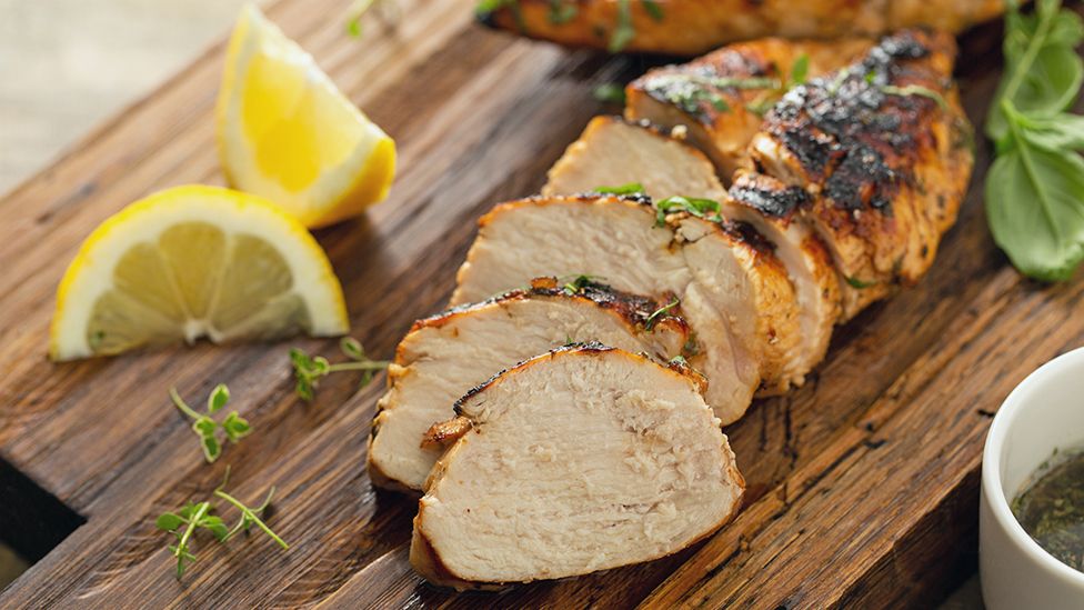 Cooked chicken breast on a chopping board with lemon and herbs