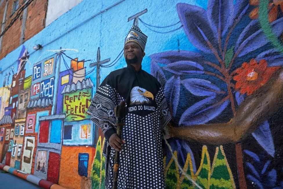 A man wearing matching a matching hat and robes stands next to a colourful street mural.