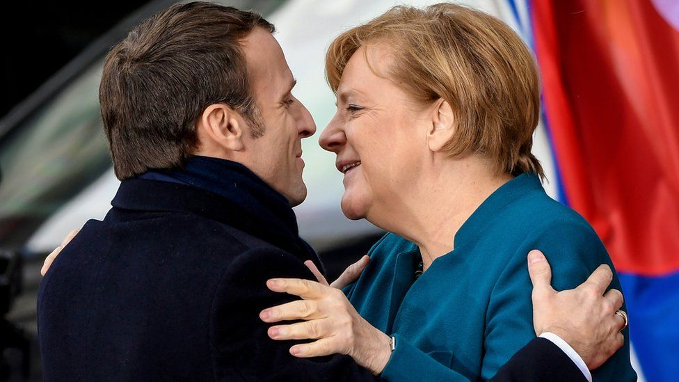 Emmanuel Macron, left, in his dark suit, hugs Angela Merkel, right, in a light blue jacket