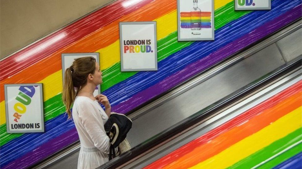 People ride a tube escalator decorated with the Pride flag colours