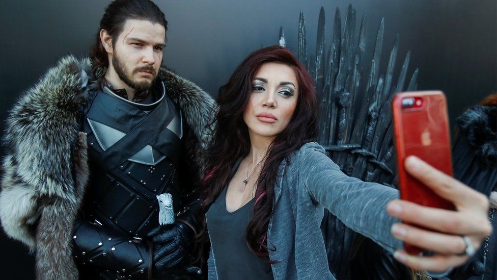 A woman shoots a selfie with an actor dressed like Jon Snow