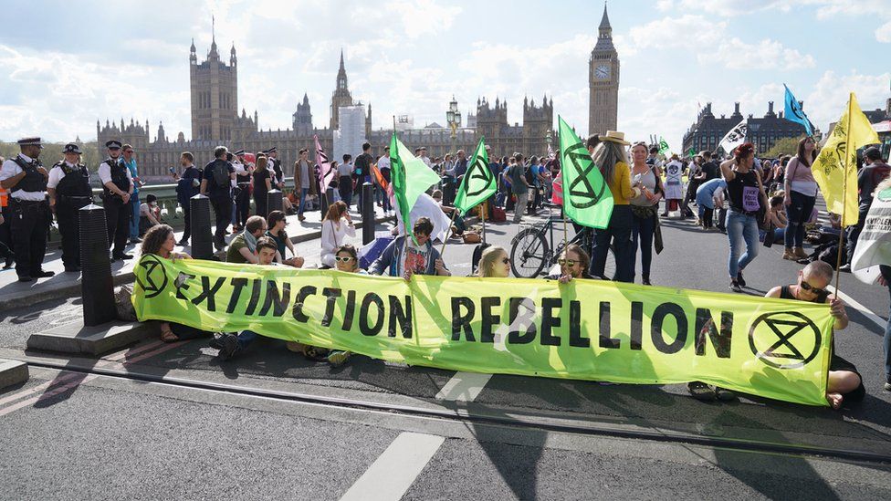 Extinction Rebellion climate protestors with flags and banners sitting on Westminster Bridge