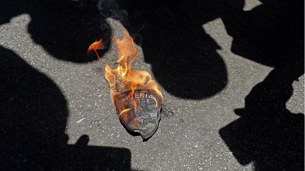 A Nigerian police emblem is seen burning during a protest outside their embassy in Pretoria