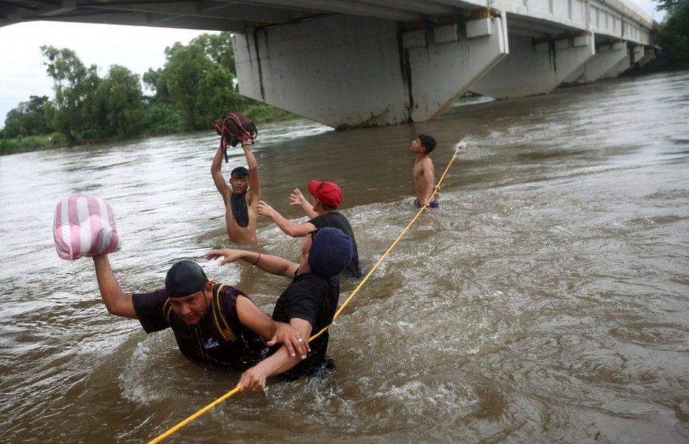 Men cross the Suchiate River with the help of rope to avoid the border checkpoint in Ciudad Hidalgo