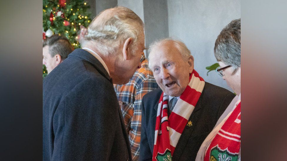 King Charles III (left) speaks to Alex Massey, aged 97, Wrexham's eldest supporter during a visit to Wrexham Association Football Club's Racecourse Ground. King Charles III and the Queen Consort met owners and Hollywood actors, Ryan Reynolds and Rob McElhenney, and players to learn about the redevelopment of the club, as part of their visit to Wrexham. Picture date: Friday December 9, 2022. PA Photo. See PA story ROYAL King. Photo credit should read: Arthur Edwards/The Sun/PA Wire