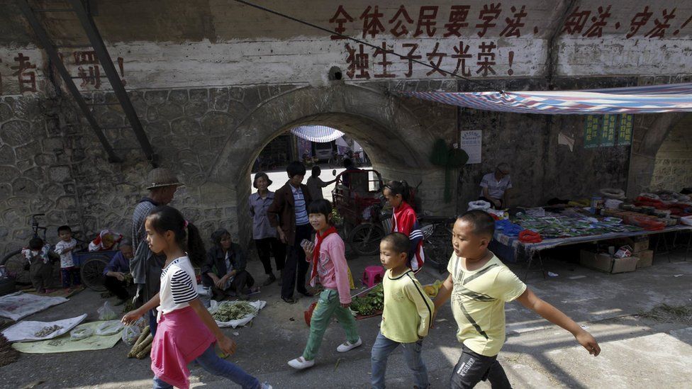 Chinese children walk past a one-child policy slogan written on a wall, which partially reads "All citizens must observe the law, a single child is glorious"