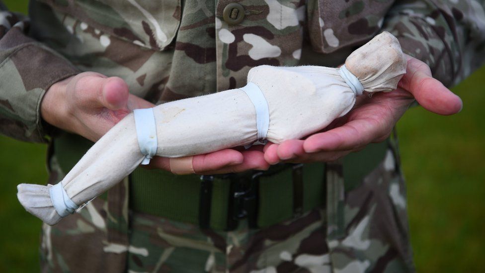 Shrouded figure held in soldiers hands