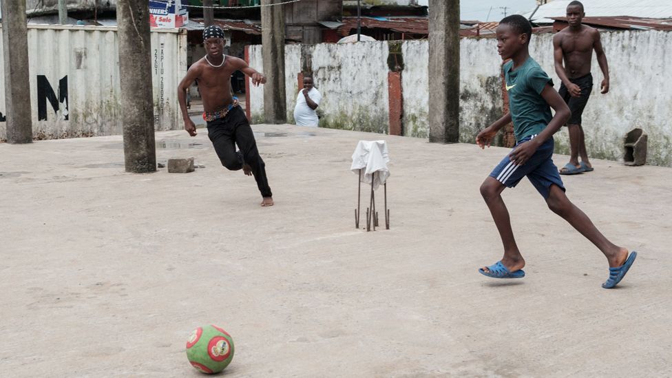 Young men play football on the ground floor of an unfinished building in Clara Town, Monrovia, Liberia - Friday 6 October 2023