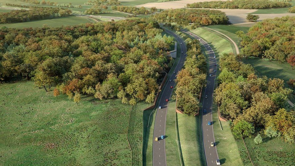 An image of the proposed Norwich Western Link road, surrounding by fields and woods. The road is lined with sloped embankments covered in grass.