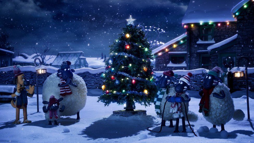 Shaun the sheep and friends looking cold around a snowy Christmas tree