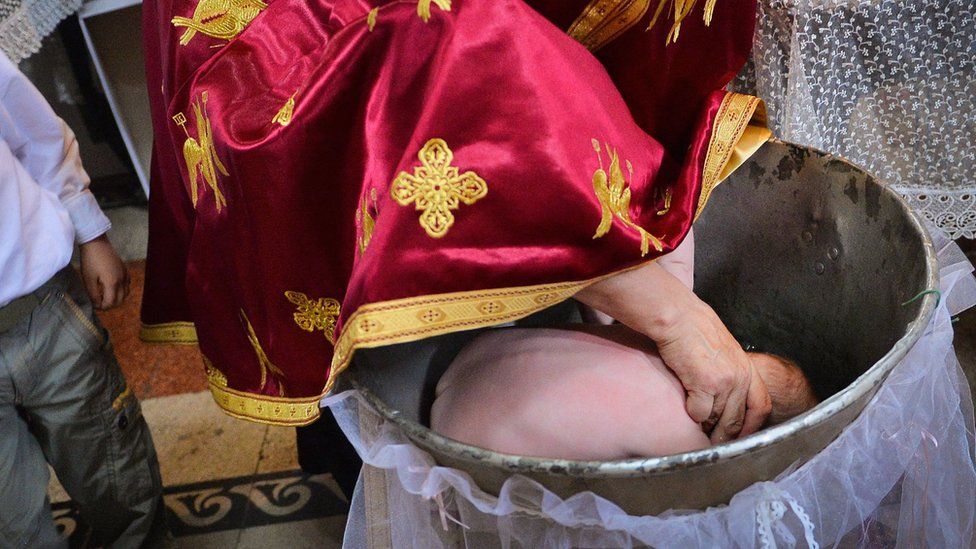 Румынский православный священник погружает голову младенца во время крещения (фото из архива)