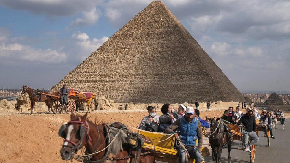 Люди едут на конных повозках у пирамид Гизы, недалеко от Каира, Египет (17 декабря 2021 г.)