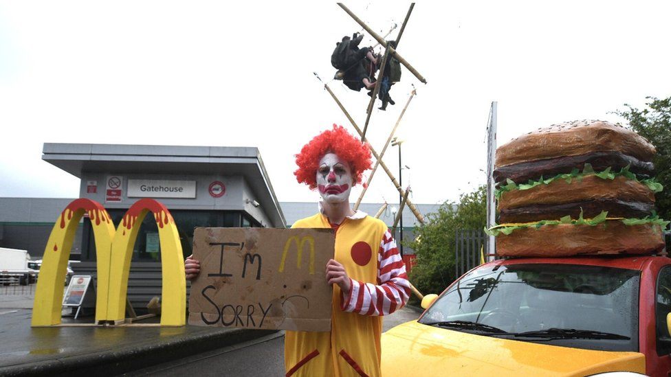An Animal Rebellion protester, dressed as a clown, and protesters suspended from a bamboo structure outside a McDonalds distribution site in Hemel Hempstead
