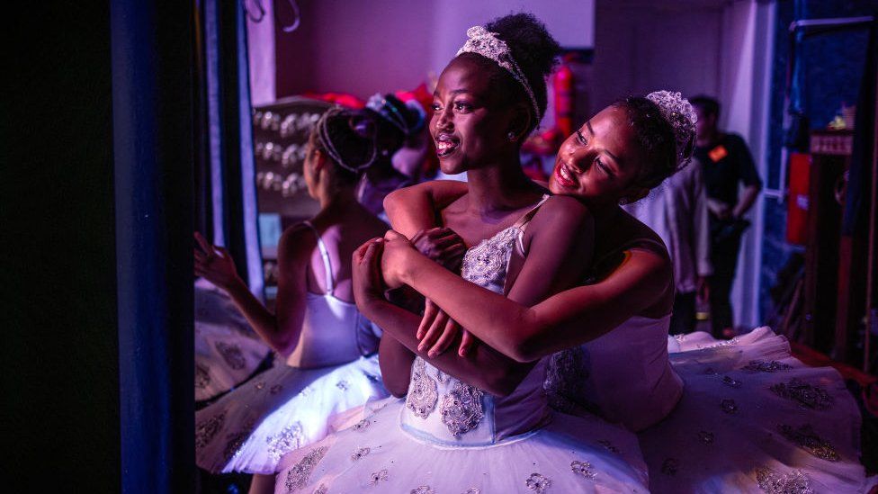 2023 оны 12-р сарын 2-нд Найроби дахь Кенийн үндэсний театрт Зул сарын баяраар тоглодог уламжлалт сонгодог балет болох "Щелкунчик" балетын тайзны ард бүжигчин Паулин Окуму (С) болон Наталья Комо (р) нар тэврэлдэж байна.