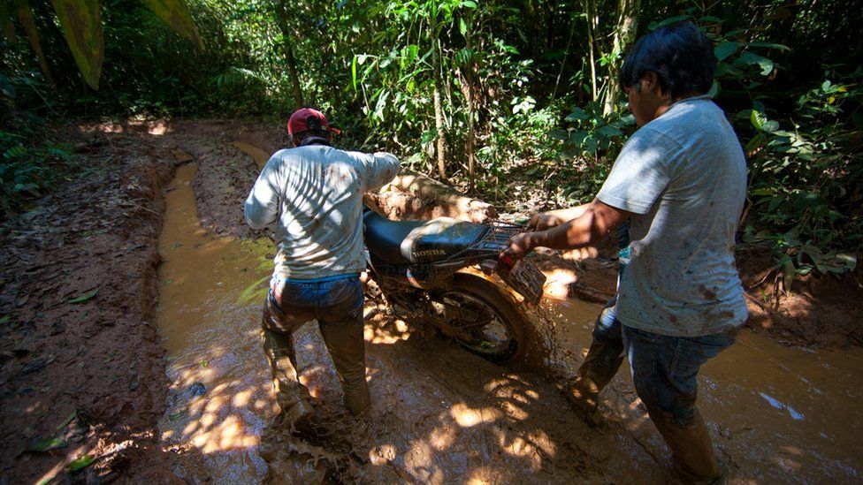 Two men are pushing a motorbike through the mud