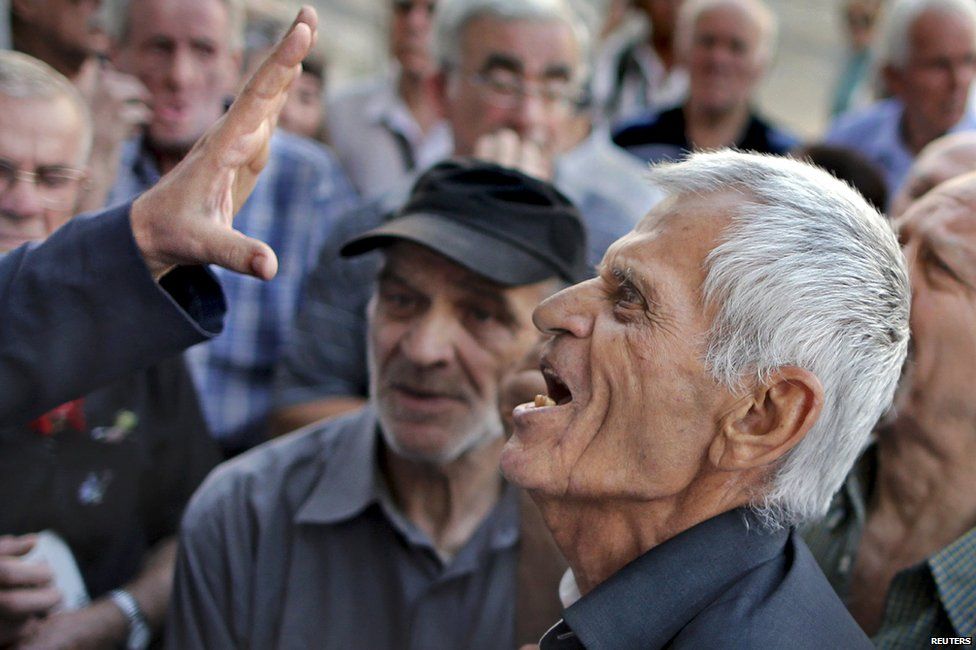 A bank employee distributes gestures to Greek pensioners seeking to withdraw €120 for the week (6 July 2015)