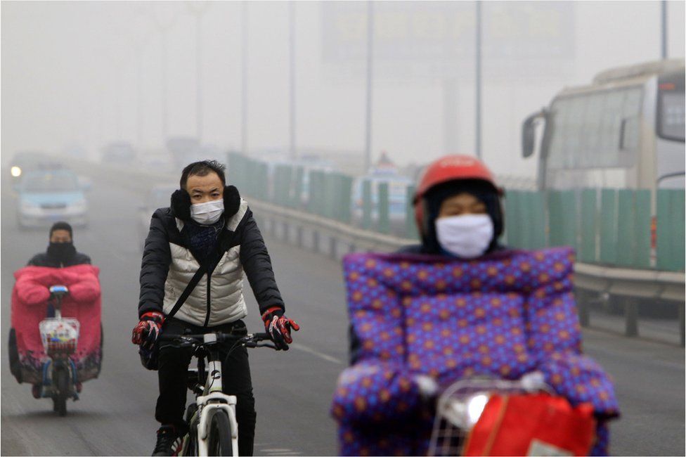 Residents wearing masks ride bicycles and electric bikes along a street amid heavy smog after the city issued its first red alert for air pollution in Tianjin, China, 23 December 2015