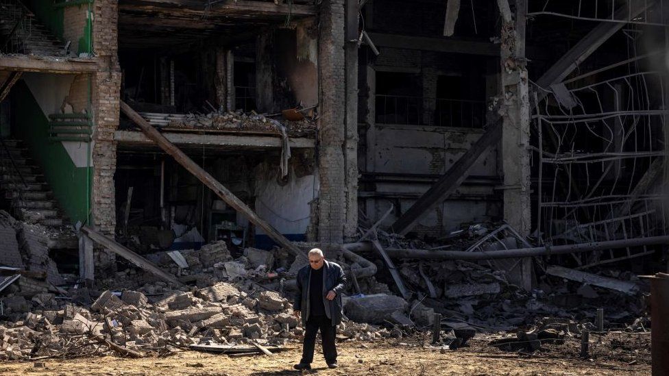 Image shows man walking among rubble