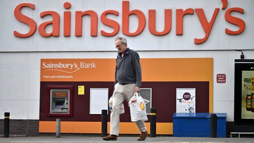 Man carrying shopping bags outside a Sainsbury's store