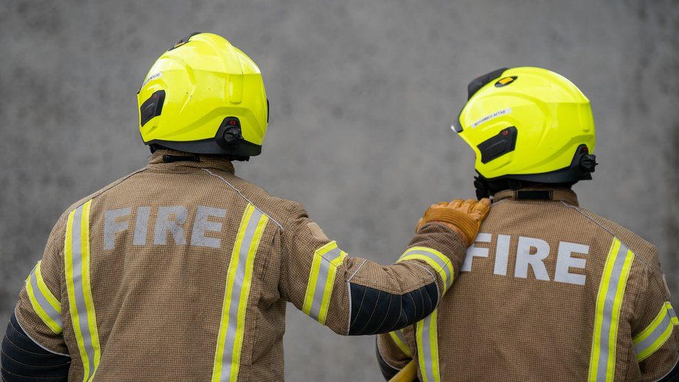 Two firemen face a wall in their uniform