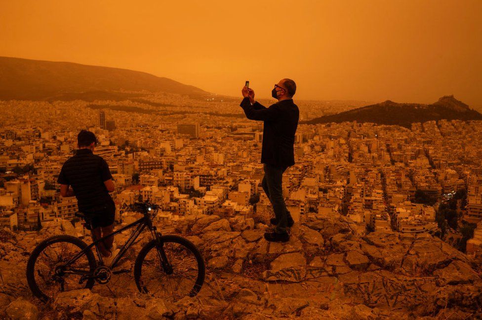 A man takes a photograph of the city of Athens from Tourkovounia hill, as southerly winds carry waves of Saharan dust to the city, in Athens, on April 23, 2024.