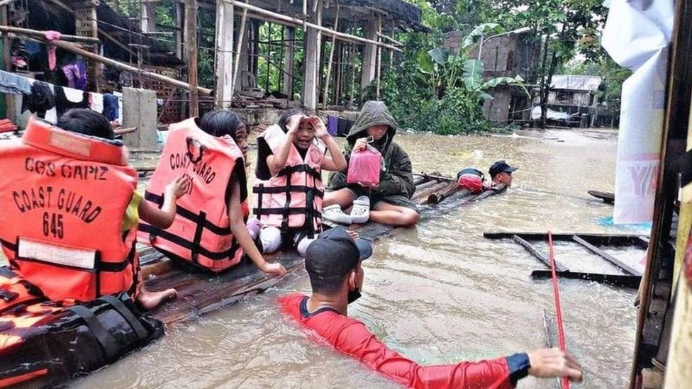 Rescue crews guide a raft carrying four people down a flooded street on Panay island