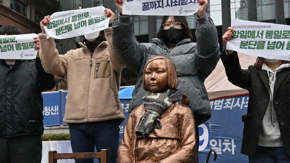 South Korean protesters hold up banners beside a statue of a teenage girl symbolising "comfort women", who served as sex slaves for Japanese soldiers during World War II, near the Japanese embassy in Seoul on March 1, 2021, the 102nd anniversary of the Independence Movement Day against the 1910-1945 Japanese colonial rule.