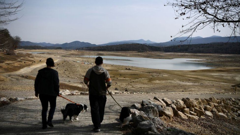 Two people walk their dogs near the partially dry Lake Montbel, south-western France, on February 21, 2023