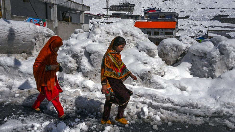 Girls walk along a snow laden street in Kalam on March 4, 2024