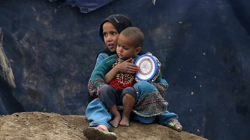 Internally displaced Afghan children sit outside their shelter in Kabul, Afghanistan