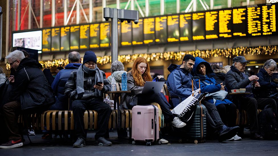 Passengers wait with luggage in front of train departure boards at King's Cross station in London on 27 December