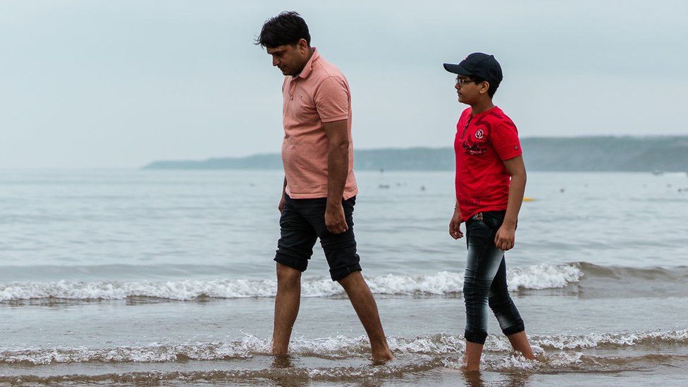 Father and son walking on the beach with the water lapping at their feet