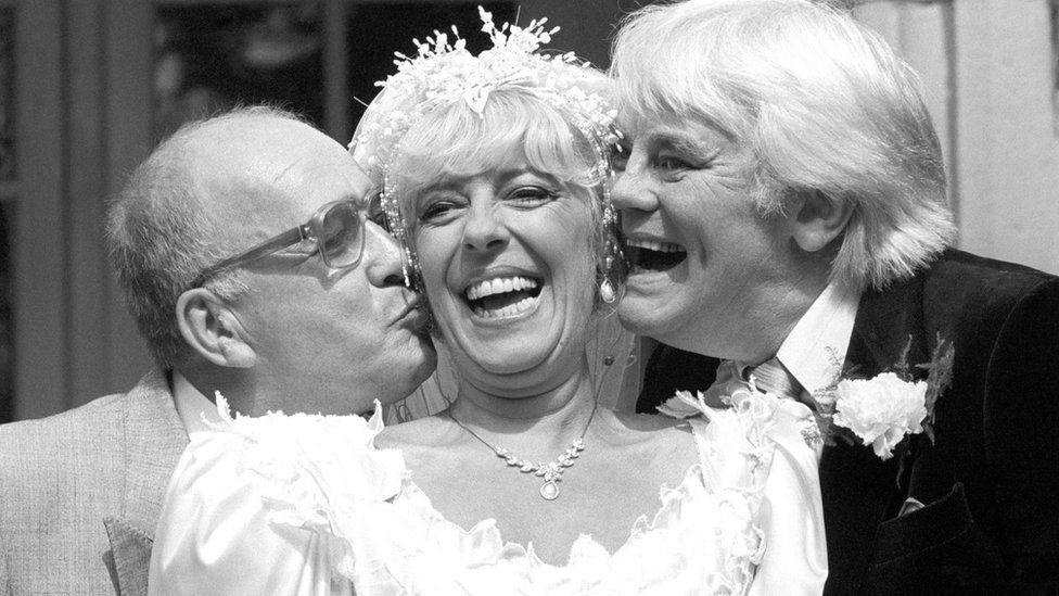 Coronation Street barmaid Bet Lynch (actress Julie Goodyear) getting a kiss from television groom Alec Gilroy (actor Roy Barraclough), and best man Charles Halliday (actor Tony Booth)