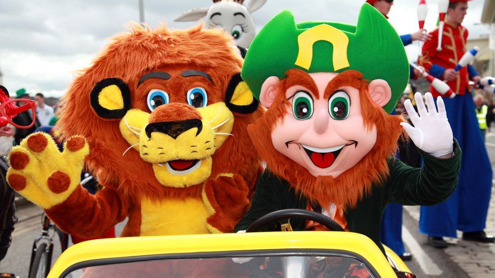 A lion and a leprechaun travel in a small yellow car during the Newry St Patrick's Day parade 2023